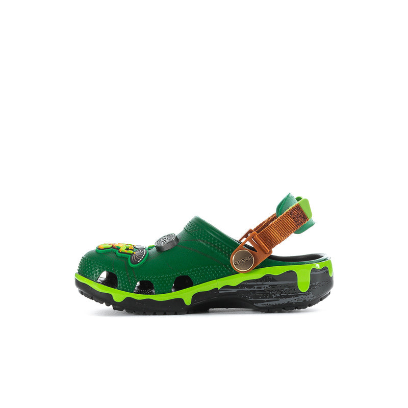 Kids green clog side view, TMNT emblem on strap, orange-brown loop and neon trim