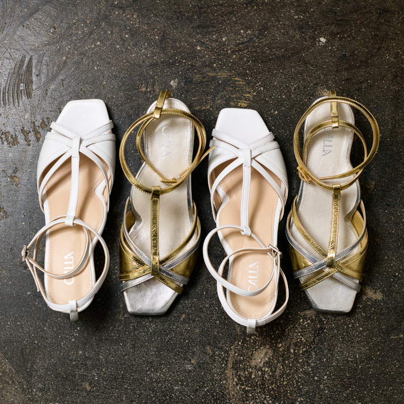 Pair of white and gold kitten-heeled sandals on a textured dark surface
