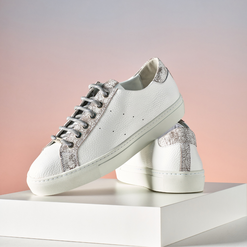 White sneakers with glittery accents on a white platform against a pink gradient background